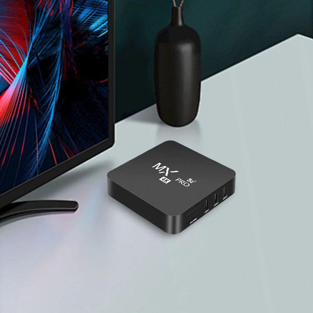 Black electronic device labeled 'MX PRO' on a white surface with a monitor in the background.